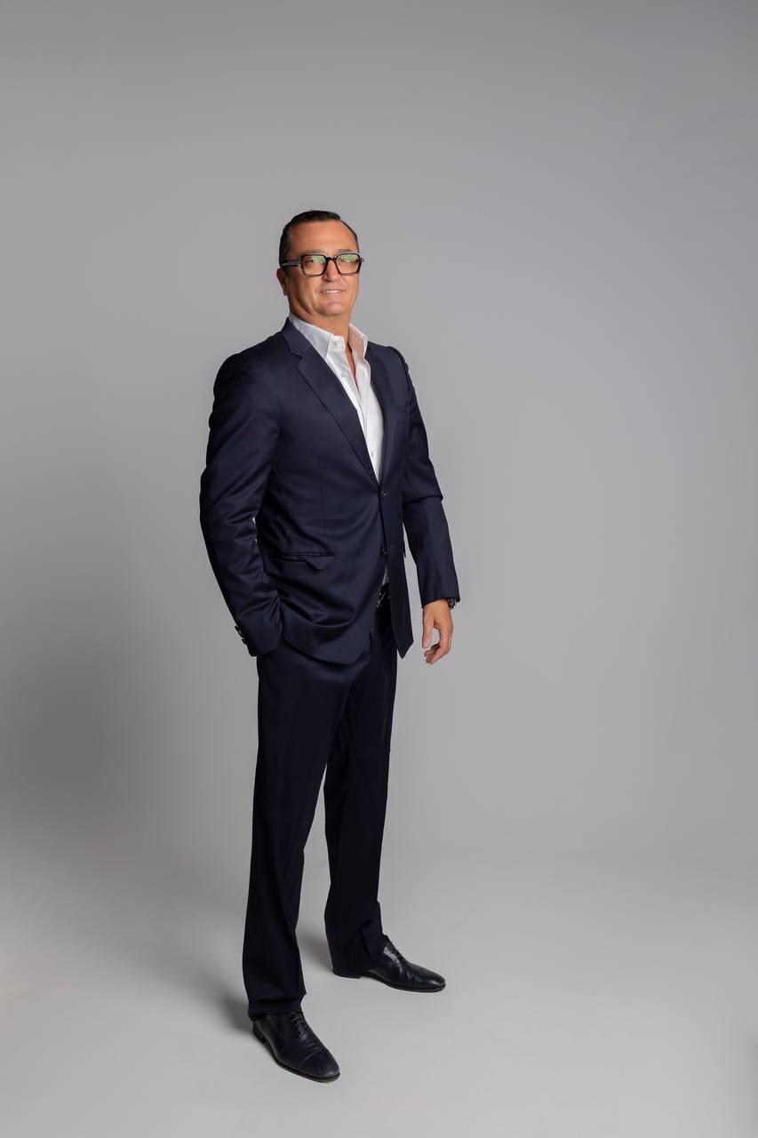 Konstantin Silver standing in a navy suit against a light grey background