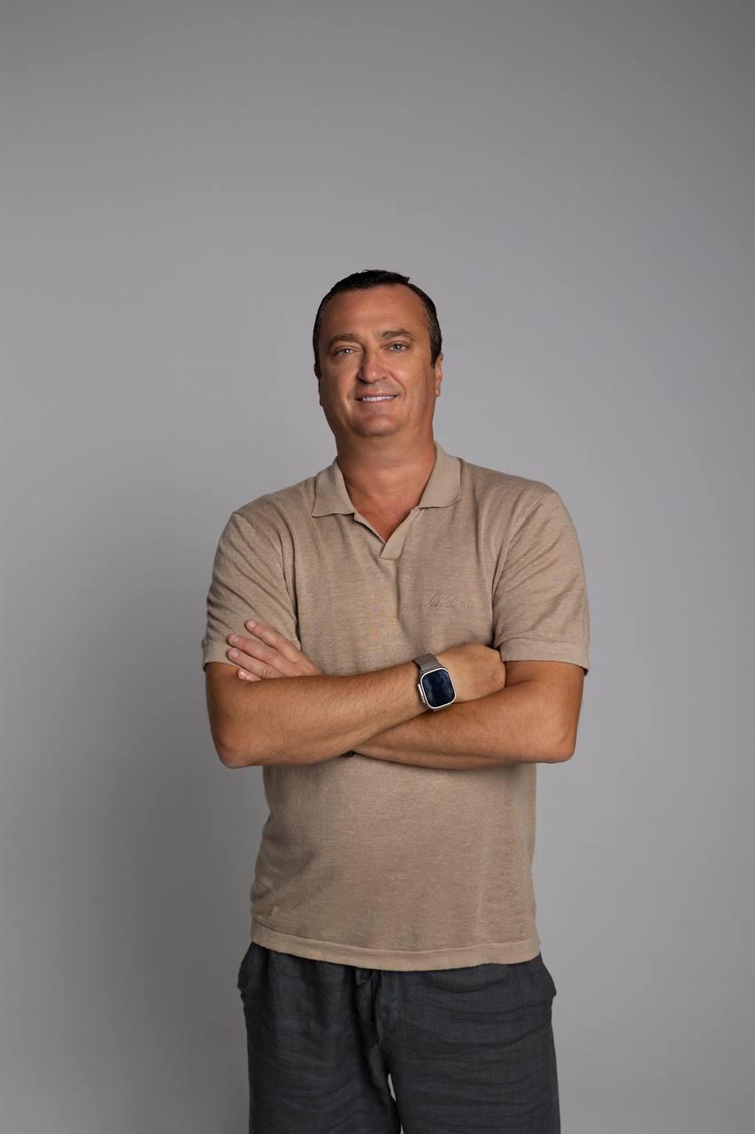 Konstantin Silver in a tan polo with arms crossed against a light grey background